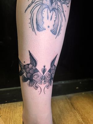 Elegant black and gray tattoo on shin featuring fish, skull, and fins. By Kiky Flore.