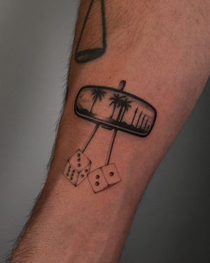 Black and gray tattoo featuring rearview mirror, palm tree, dice by Ophelya Jeandat. Chicano style with illustrative details.