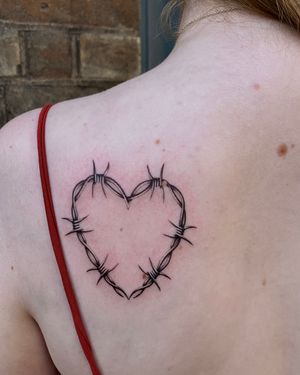 Black and gray micro realism tattoo featuring a heart intertwined with barbed wire and thorns by artist Ophelya Jeandat.