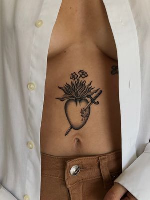Neo-traditional stomach tattoo featuring a heart and sword motif by Ophelya Jeandat. Bold and vibrant traditional style.