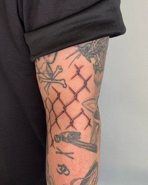 Black and gray illustrative tattoo of a chain fence created by Ophelya Jeandat, featuring intricate dotwork detailing.