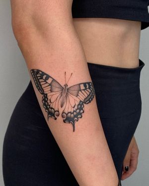 Elegant black and gray butterfly tattoo on lower arm by Ophelya Jeandat. A symbol of beauty and transformation.