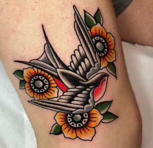 Get inked with a classic design by Barney Coles featuring a beautiful swallow and vibrant flower. Perfect for lovers of traditional tattoo styles.