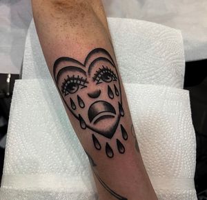Embrace your emotions with this striking tattoo by artist Barney Coles, featuring a heart and crying sad face motif in traditional style.