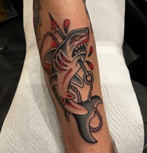 Get inked with a traditional style forearm tattoo featuring a menacing shark and harpoon by artist Barney Coles. Dive deep into this timeless design today!