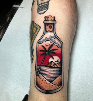 Embrace the serene beauty of a traditional illustrative tattoo featuring a sunset, beach, bottle, and palm tree by the talented artist Barney Coles.
