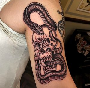 Stunning arm tattoo featuring a traditional style snake and skull motif by Barney Coles. Perfect blend of dark and powerful imagery.