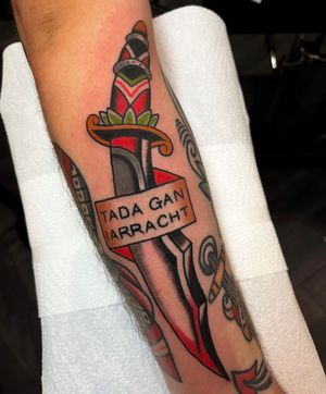 Explore the bold and timeless design of a dagger and banner tattoo on your forearm by tattoo artist Barney Coles.