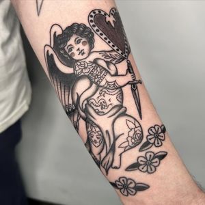 This stunning black and gray traditional tattoo features an angelic cherub, expertly executed by the talented artist Claudia Trash.