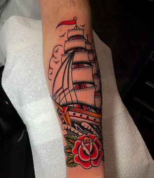 Enjoy the timeless beauty of this traditional tattoo featuring a sea, flower, rose, ship, and boat motif by the talented artist Barney Coles.