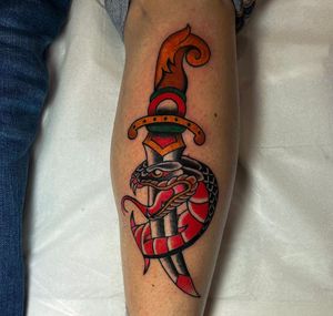 A bold traditional tattoo featuring a fierce snake entwined around a sharp dagger, expertly inked by Barney Coles on the calf.