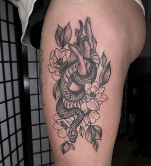 Upper leg tattoo by Barney Coles featuring a snake, flower, hand, and leaves in a black and gray floral style.