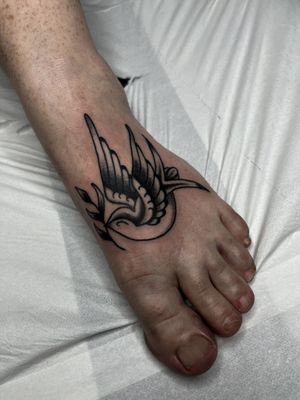Capture the timeless charm of a traditional swallow tattoo on your foot by Barney Coles. Fly high with this classic design!