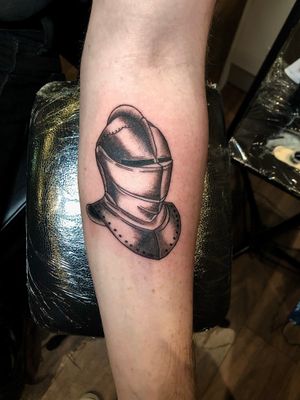A stunning black and gray illustrative tattoo of an armor helm, expertly done by Claudia Whiteheart. Detailed and impressive design.