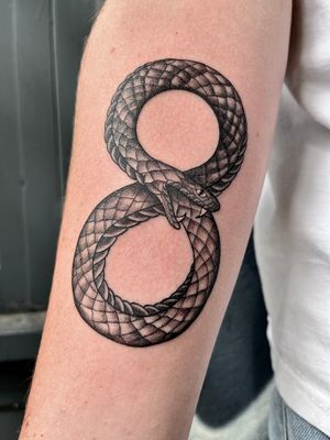 A mesmerizing black and gray illustrative tattoo of an infinity snake consuming its own tail, symbolizing eternity and cycles of life. Designed by the talented artist Claudia Whiteheart.