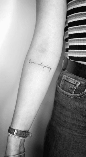 Fine line tattoo featuring 'serendipity' in elegant cursive lettering by Math. Perfect for those who believe in fate and happy accidents. Small yet meaningful.