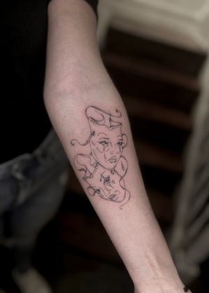 Illustrative tattoo by Maddie featuring a delicate fine line design of a theater mask