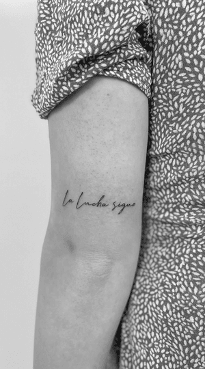 Math's fine line tattoo features small cursive lettering of 'La Lucha Sigue', symbolizing perseverance in a graceful manner.