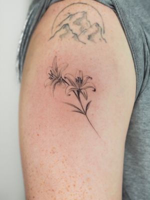 Elegant black and gray fine line floral tattoo of a lily by renowned artist Oscar Jesus. Botanical perfection.