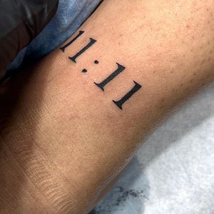 Get a unique lettering tattoo of the number 11:11 representing a special time or date. Done by the talented artist Seven.