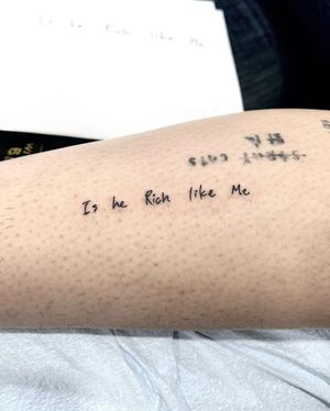 Get a minimalist and elegant fine line tattoo with small lettering of 'Is He Rich Like Me' by the talented artist Seven.