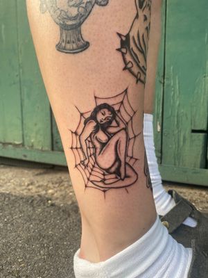 Get inked with a timeless traditional tattoo featuring a sultry pin up girl entwined in a spiderweb, expertly crafted by Charlie Macarthur.