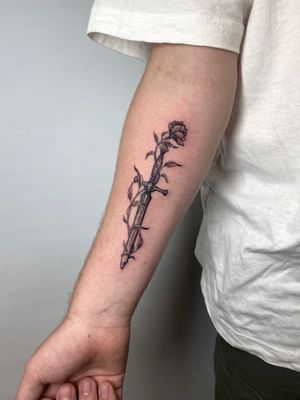 Illustrative tattoo combining a delicate flower with a sharp sword, by Liam Collins.