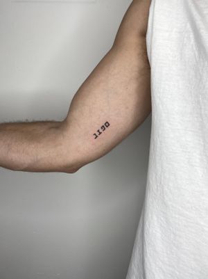 Get a unique and personalized small lettering tattoo on your upper arm by talented artist Liam Collins. Perfect for making a subtle yet meaningful statement.