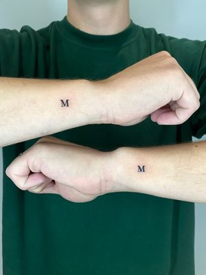Small lettering tattoo of the letter 'm' by artist Liam Collins, perfect for subtle wrist placement.