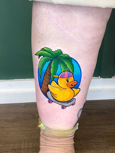 Unique illustrative tattoo featuring a beach scene with a rubber duck, skateboard, and palm tree. By artist Liam Collins.