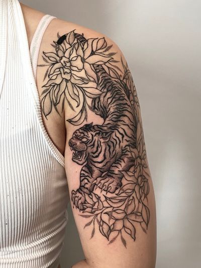Intricate Japanese style upper arm tattoo featuring a fierce tiger and delicate peony flowers, created by artist Liam Collins.