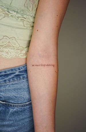 Small lettering tattoo by Gabriele Edu, reminding us to keep moving forward and never stop dancing in life.
