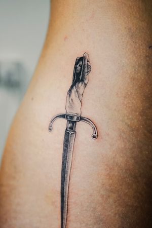 Captivating micro-realism tattoo by Gabriele Edu featuring a dagger and a powerful woman in black and gray illustrative style.
