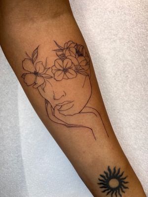 Elegant forearm tattoo by Claudia Whiteheart featuring a delicate flower and a serene woman's face in fine line style.