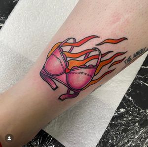 Unique lower arm tattoo by Katy Sarsfield, combining feminine lingerie with fierce flames in a modern neo-traditional style.