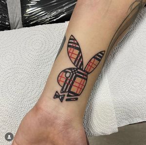 Unique tattoo by Katy Sarsfield featuring a playful playboy bunny motif intertwined with a stylish plaid pattern.