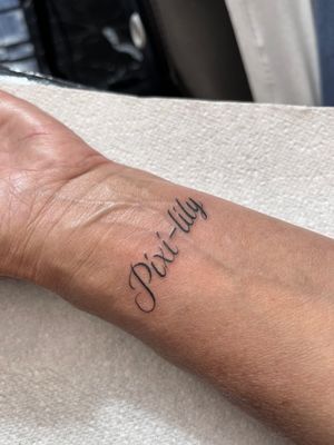 A delicate small lettering tattoo designed by Claudia Whiteheart, placed on the wrist for a subtle and elegant touch.