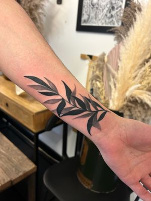 An intricate black and gray dotwork tattoo of a branch with leaves, expertly done by Jack Howard on the forearm.