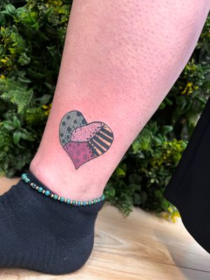 Unique ankle tattoo by Rachel Angharad featuring a heart, stitch, and patch motifs in a neo-traditional style.