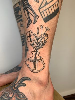 Elegant fine-line tattoo featuring a beautiful vase with intricate flowers and plants, by the talented artist Dan Bramfitt.