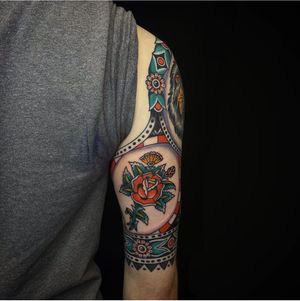 Get a beautiful traditional rose tattoo on your upper arm by talented artist Sam Young. Timeless and classic design.