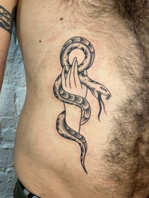 Capture the mesmerizing beauty of a snake intertwining with a hand in this traditional style tattoo by Rachel Arfin.