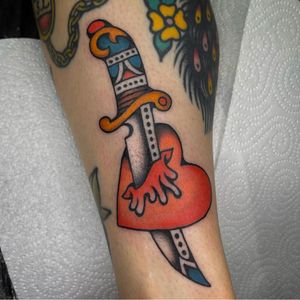 Classic lower leg tattoo featuring a heart pierced by a dagger, expertly done in traditional style by renowned artist Sam Young.
