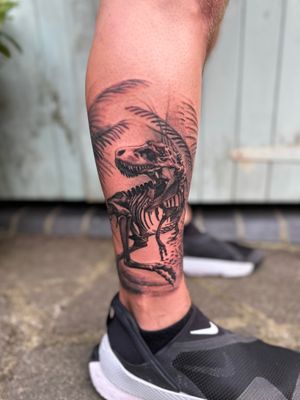Explore the ancient world with this striking black and gray tattoo of a dinosaur skeleton, expertly done by Joni Smith.