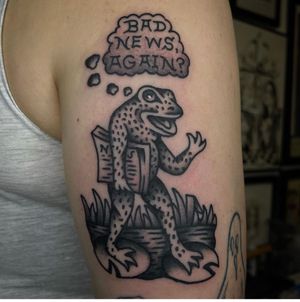 Get a unique traditional tattoo featuring a frog and newspaper motif crafted by the talented artist Sam Young. Stand out with this quirky design!