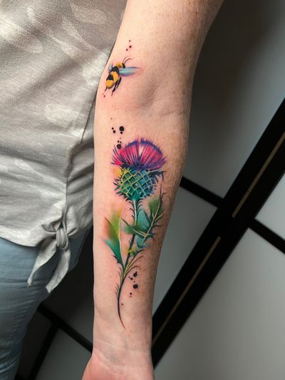 Transform your forearm into a colorful canvas with this stunning watercolor tattoo of a bee and flower by Cloto.tattoos. Stand out with this unique and vibrant design!