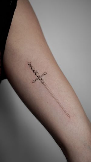 Get a sleek and stylish sword tattoo on your upper arm with fine line details by the talented artist Jacky Yang.