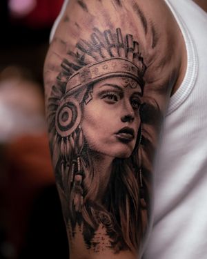 Capture the beauty and strength of a Native American woman wearing a traditional war bonnet in this stunning black and gray realism tattoo by Abel Lopez.