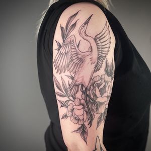 This stunning illustrative tattoo features a graceful crane surrounded by intricate floral designs, expertly done by tattoo artist Paula.