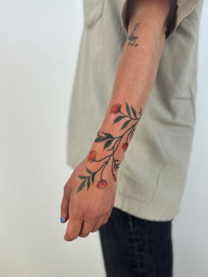 Adorn your skin with a beautiful botanical masterpiece by artist Paula. This tattoo features intricate floral details on a graceful branch.